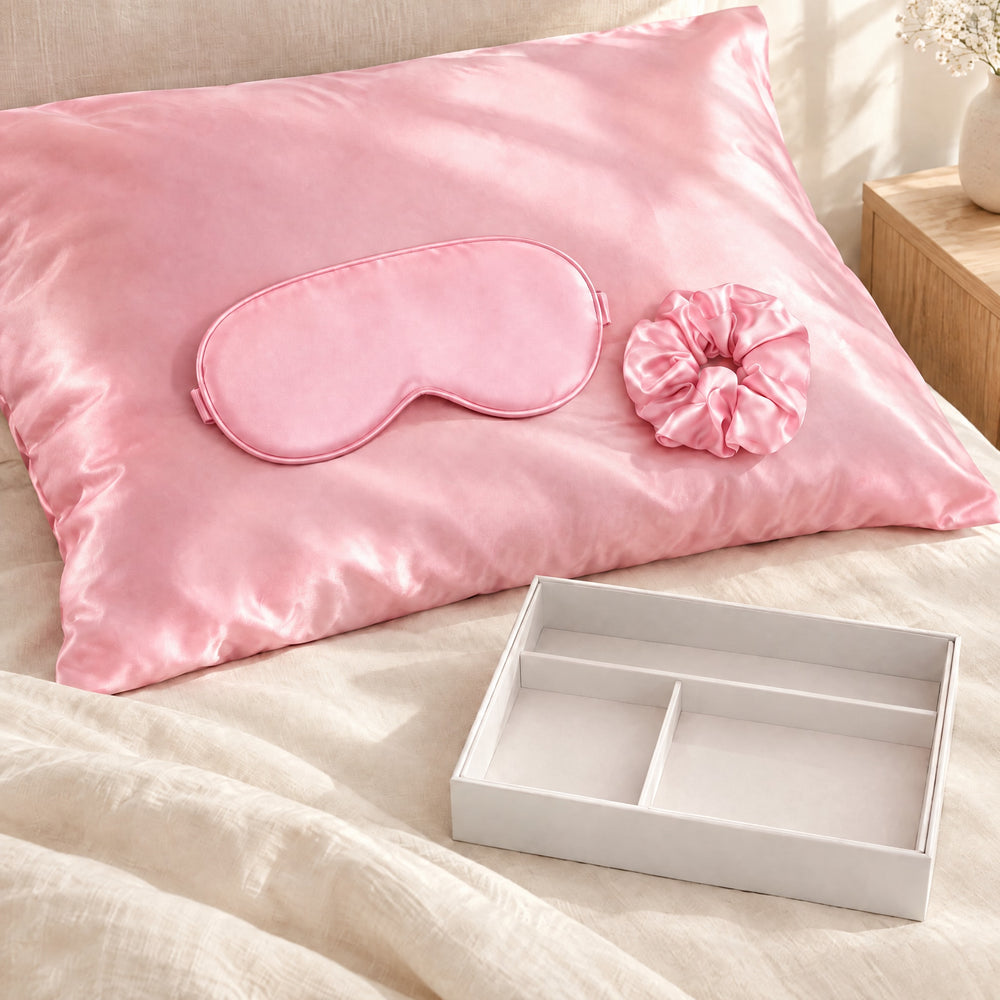 RosyIron pink satin pillowcase on a bed pillow with the matching sleep mask and scrunchie
