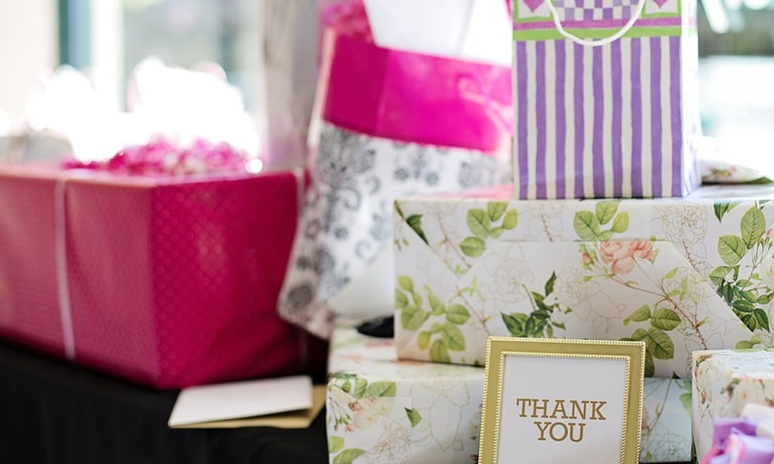 Wrapped bridal shower gifts in pink, lilac and floral paper stacked on a table with a gold Thank You frame