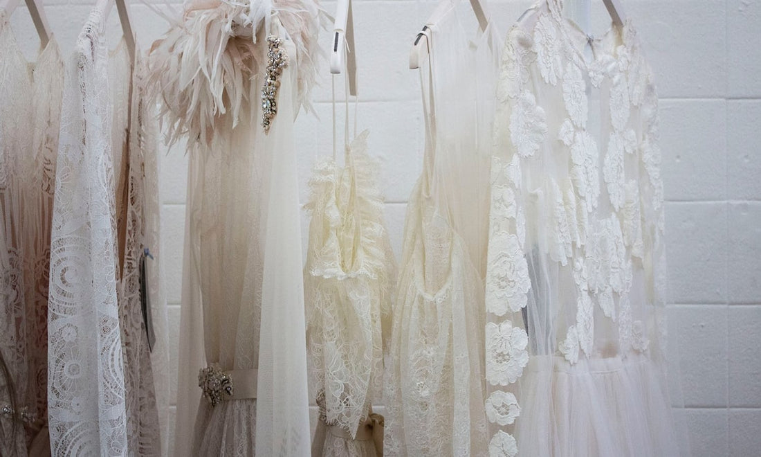 White tulle and lace dresses hanging on a rail against a white brick wall