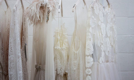 White tulle and lace dresses hanging on a rail against a white brick wall