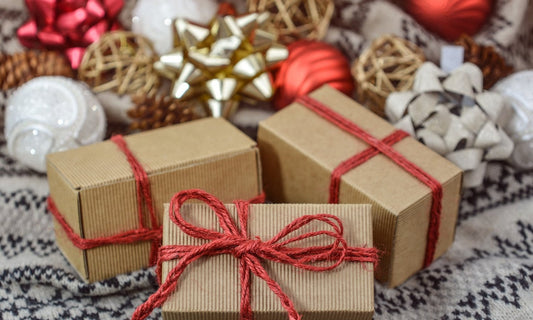 Three kraft paper gift boxes tied with red twine on a knit sweater with Christmas bows and ornaments