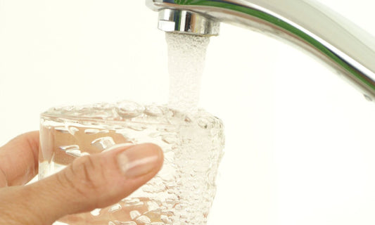Hand filling a glass with tap water from a chrome kitchen faucet