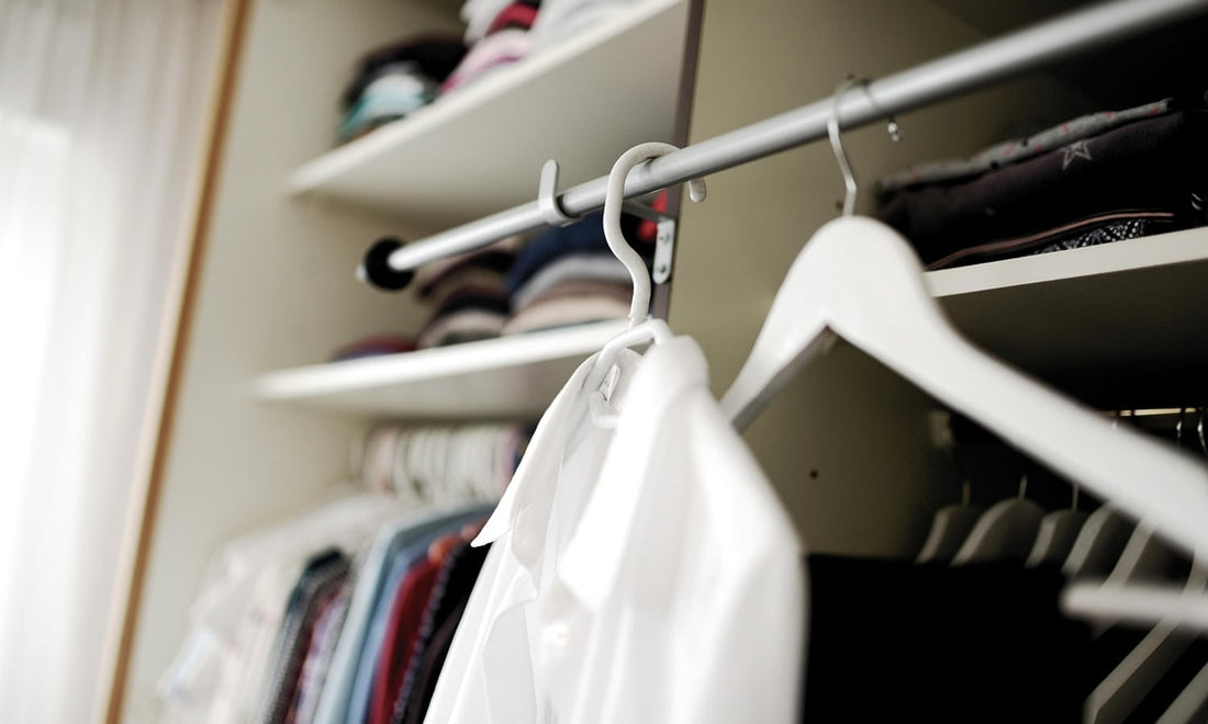 White shirt on a white hanger on a closet rail with folded clothes on the shelves behind