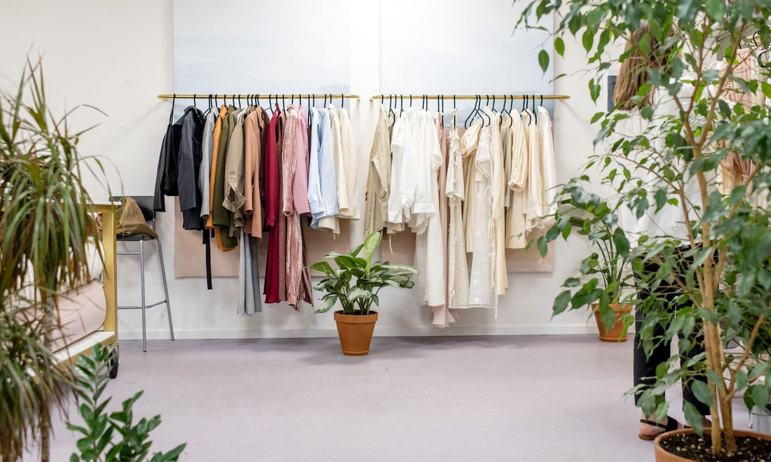 Blouses, shirts and dresses hanging on a rail in a bright studio with plants