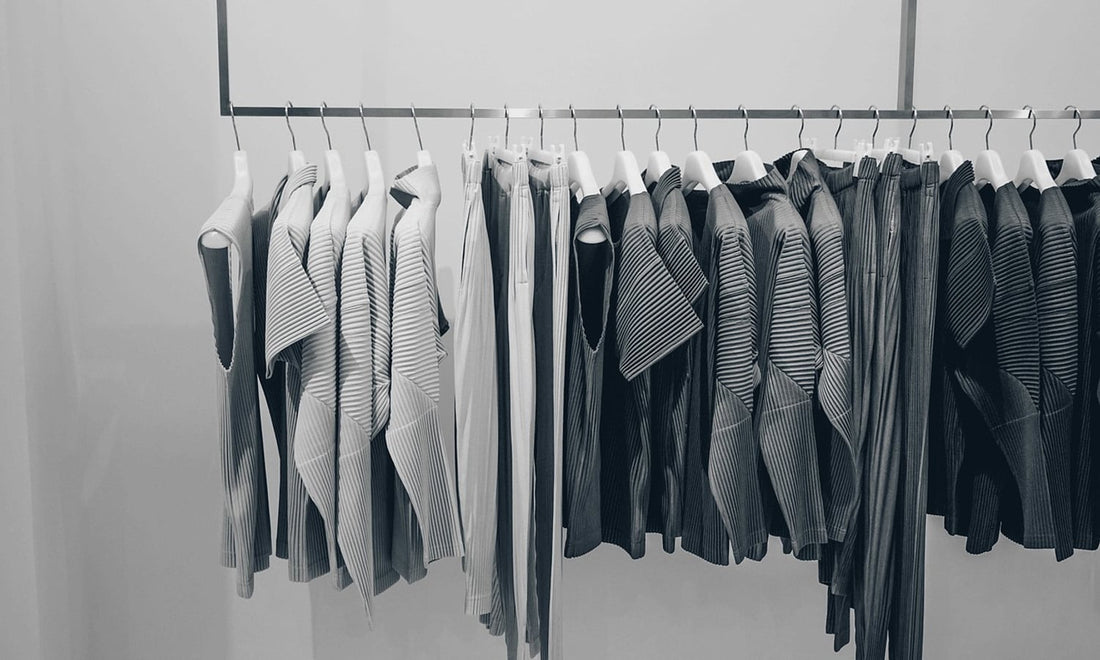 Rack of finely pleated tops and trousers in grey tones on white hangers