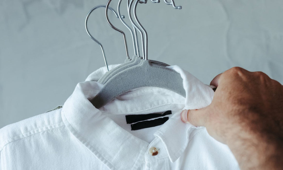Hand straightening the collar of a white dress shirt on a hanger