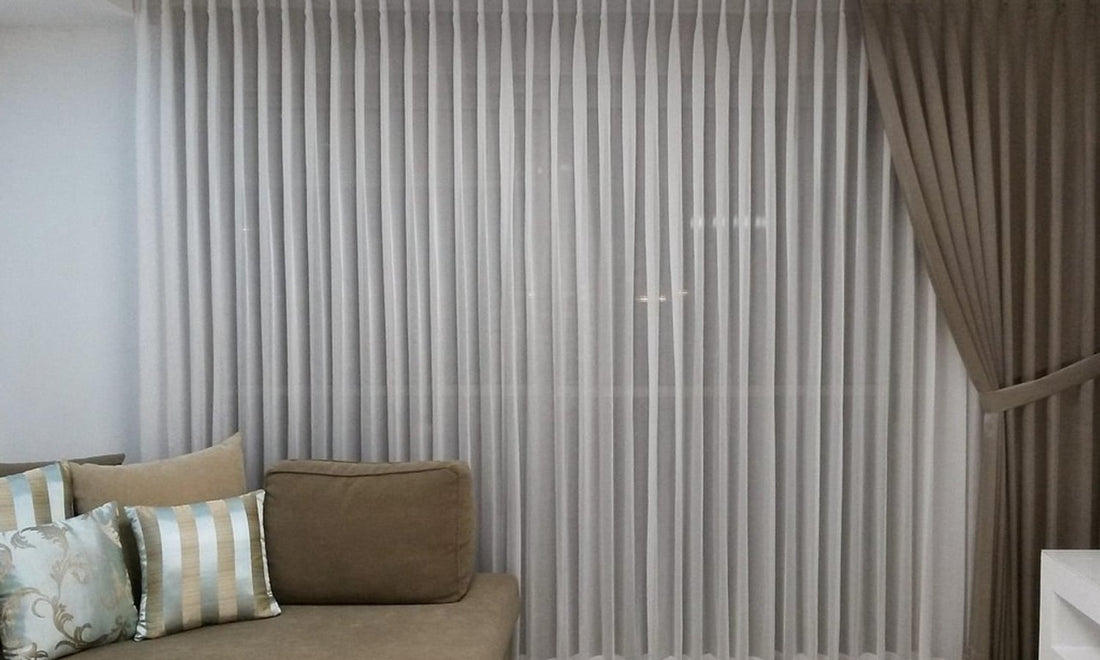 White sheer curtains and taupe drapes hanging in a living room behind a sofa