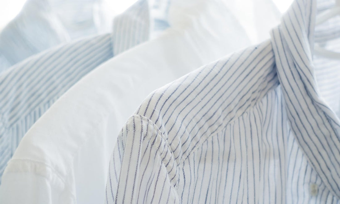 White and blue striped cotton shirts hanging on white hangers in soft daylight