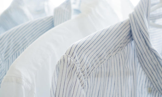 White and blue striped cotton shirts hanging on white hangers in soft daylight