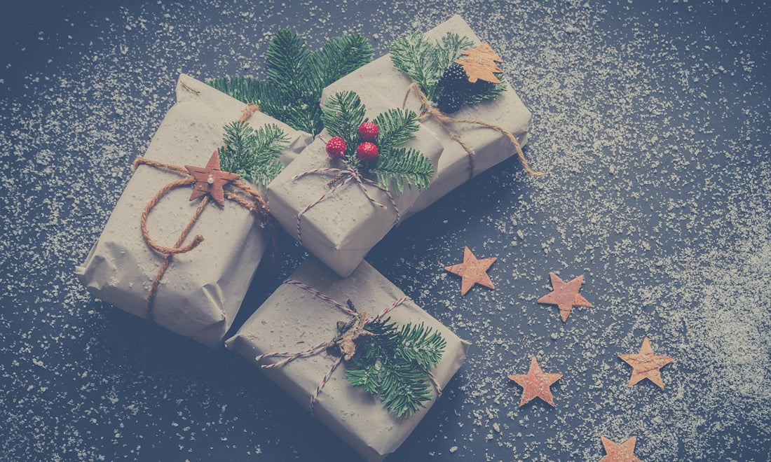 Small Christmas gifts wrapped in plain paper with twine, pine sprigs and wooden stars on a dark surface