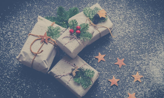 Small Christmas gifts wrapped in plain paper with twine, pine sprigs and wooden stars on a dark surface