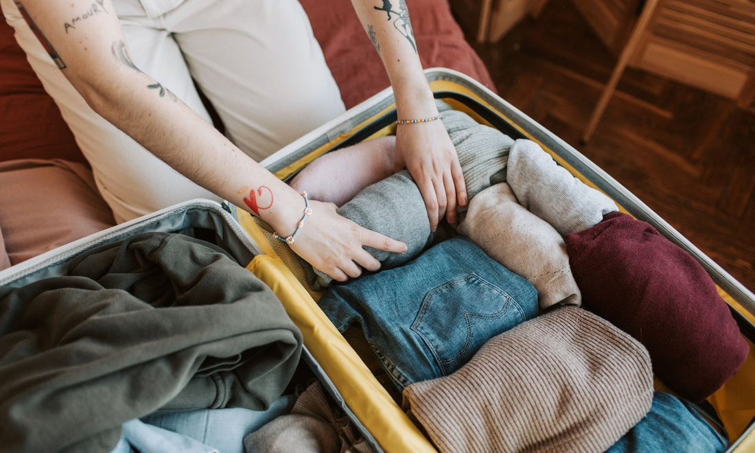 Hands packing rolled sweaters and jeans into an open suitcase before a trip