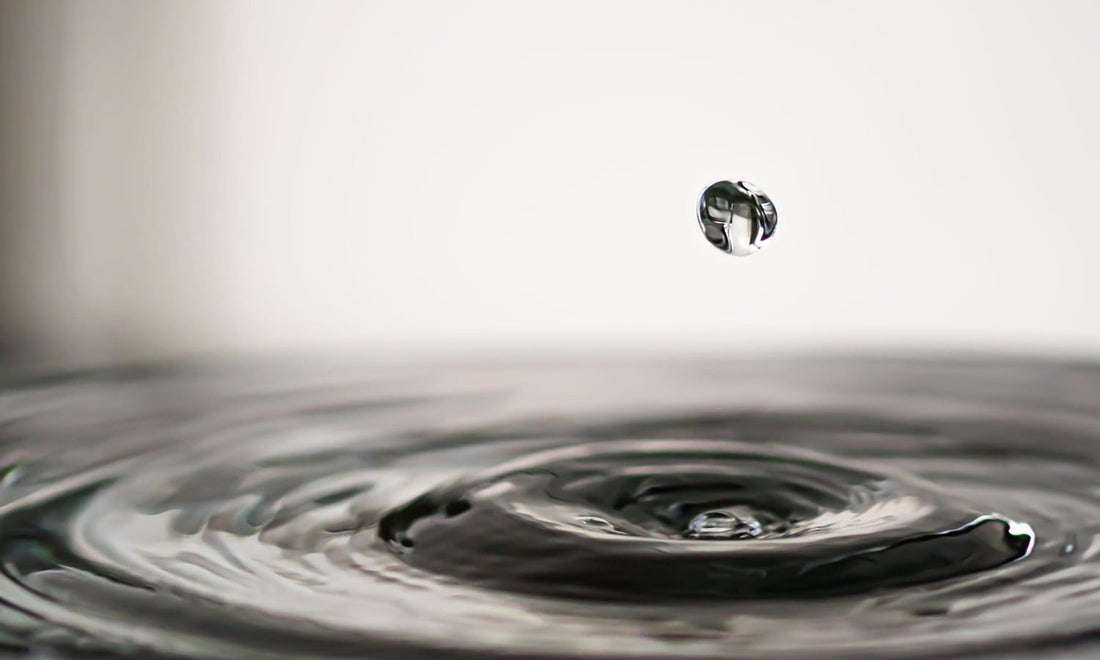 A single drop of water falling into a still pool, with ripples spreading out