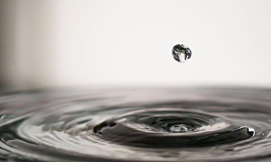 A single drop of water falling into a still pool, with ripples spreading out