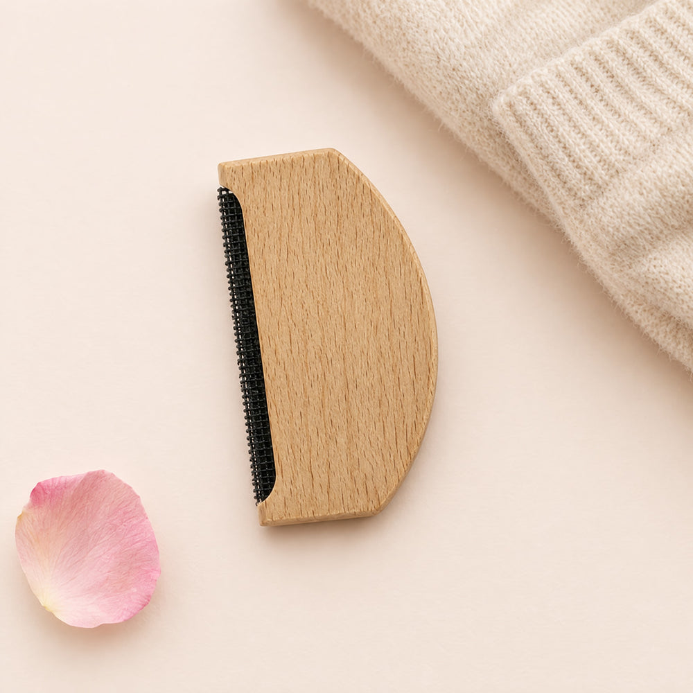 RosyIron cashmere comb, a half-moon natural wood sweater comb with a fine black mesh strip, on a blush backdrop