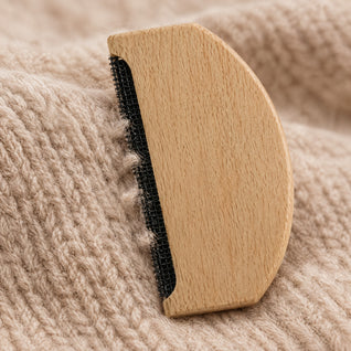 RosyIron cashmere comb close-up showing the fine black mesh strip lifting fuzz from an oatmeal knit