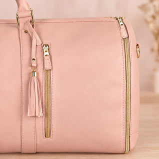 RosyIron garment duffel close-up of pink PU, gold zipper front pocket, D-ring handle and leather tassel