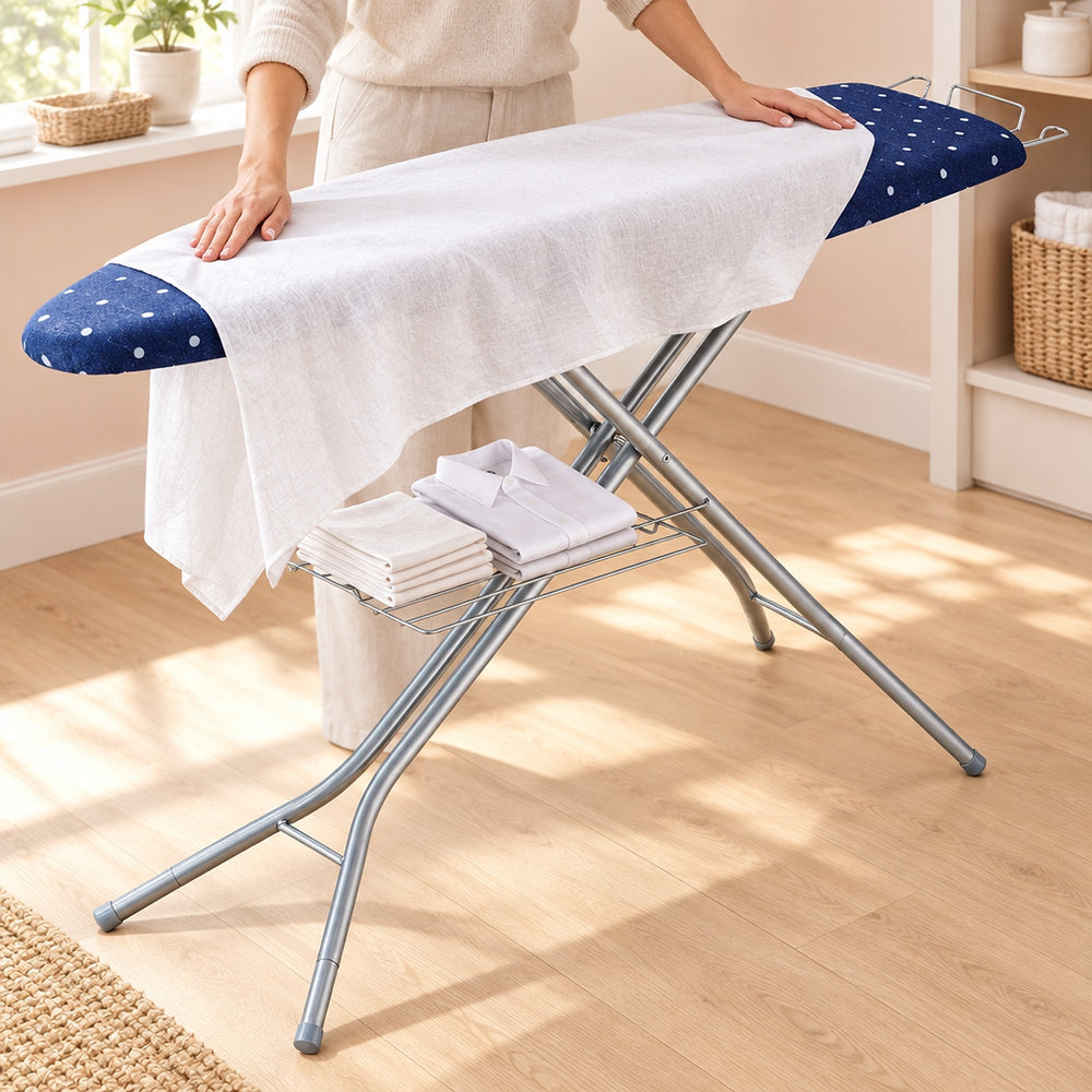 RosyIron ironing board in a laundry room, hands smoothing a linen tablecloth, folded napkins on the tray