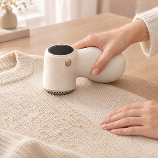RosyIron fabric shaver removing pills from a cream knit sweater on a light wood table