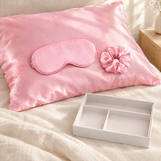 RosyIron pink satin pillowcase on a bed pillow with the matching sleep mask and scrunchie