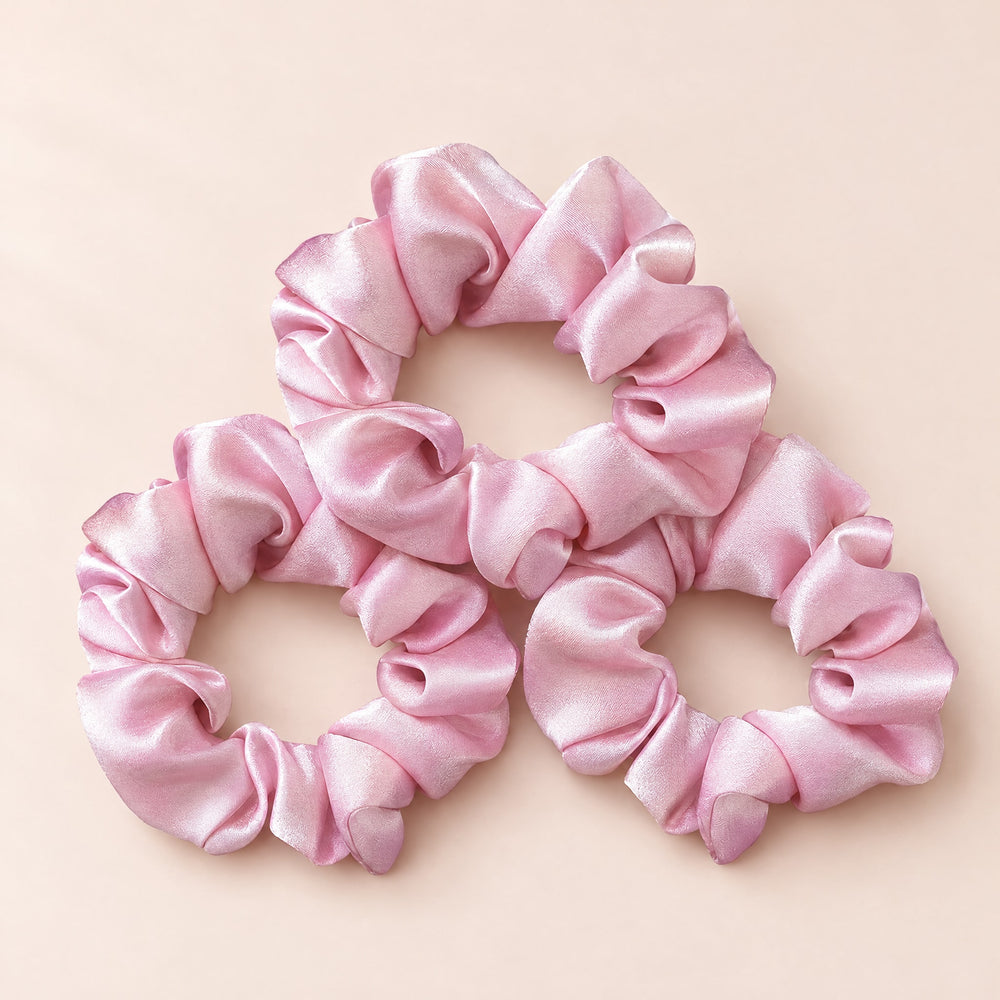 RosyIron pink scrunchies, three soft satin-look hair ties overlapping on a blush-cream backdrop