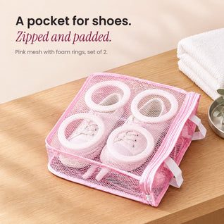 RosyIron pink mesh shoe wash bag holding small white canvas sneakers on a wood shelf beside folded towels