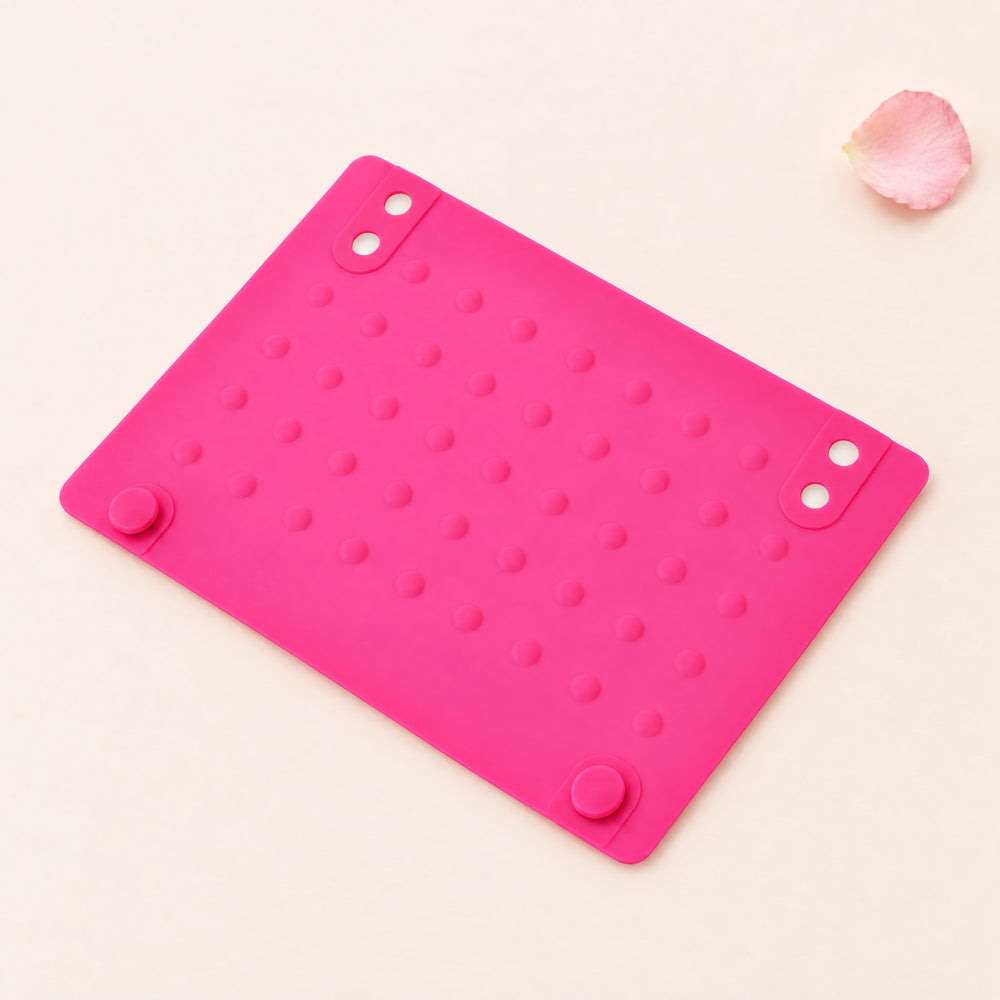 RosyIron silicone heat-resistant mat in pink with raised dots lying flat on a blush-cream backdrop