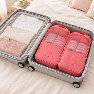 RosyIron pink travel shoe bags packed in an open suitcase beside folded shirts and sweaters on a bed