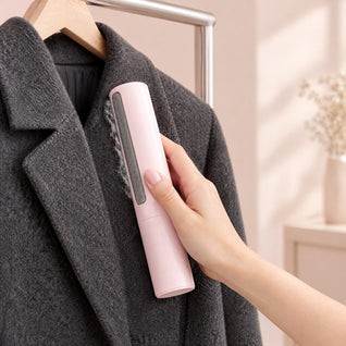 RosyIron pink lint brush held in hand, brushing lint off a charcoal wool coat hanging on a wooden hanger